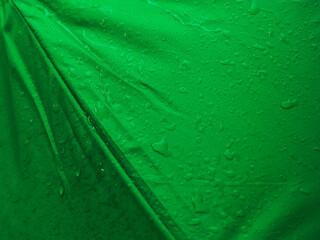 Green umbrella texture and water drops for close-up rainy season background.