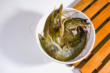 three fresh prawns served in a white porcelain bowl on a wooden coaster