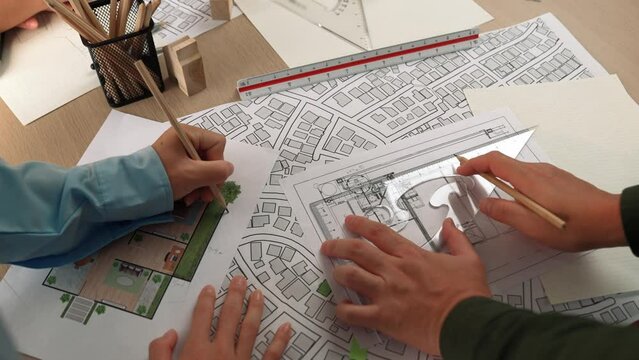 Smart architect and safety engineer discussion about building blueprint on table with architectural document, measurement tools and wooden block scatter around at modern office. Closeup. Delineation.