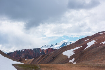 Scenic view to high alpine valley between glacier and big hill against large snowy peak far away in...