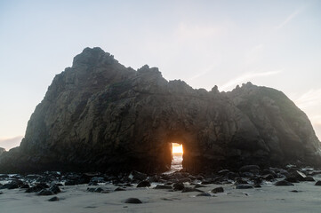 Wide-angle shot of the keyhole arch at Pfeiffer beach, California, whit the setting sun peeping...