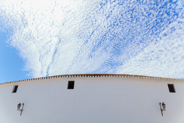 white facade of a bullring with a blue sky with clouds