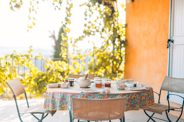Outdoor breakfast setting on terrace, blur grape leaves blossoms. Cozy romantic tranquil table...