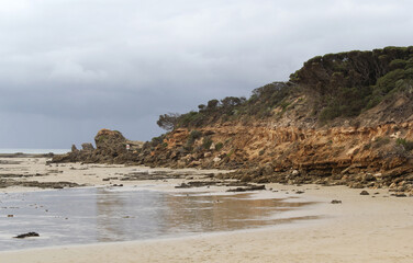 Beach, ocean and rugged cliffs under an overcast sky at Point Roadknight on the Great Ocean Road in...