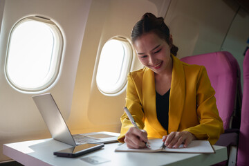Attractive Asian businesswoman passenger sits on a business class luxury plane while taking notes...