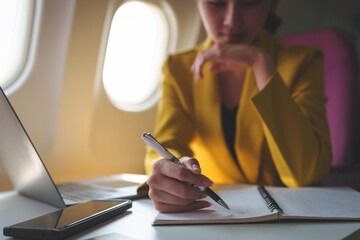 Attractive Asian businesswoman passenger sits on a business class luxury plane while taking notes...