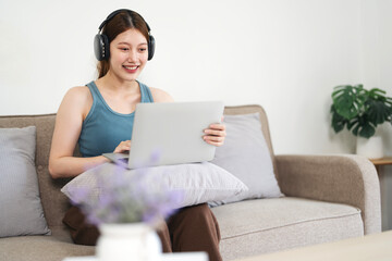 Image of young  happy cheerful cute  woman sit indoors at home using laptop computer working and listening music with earphones.