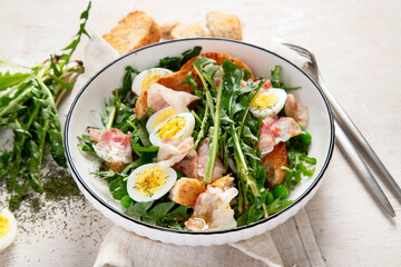 Summer fresh salad from dandelion leaves, eggs, bacon and with bread on light background