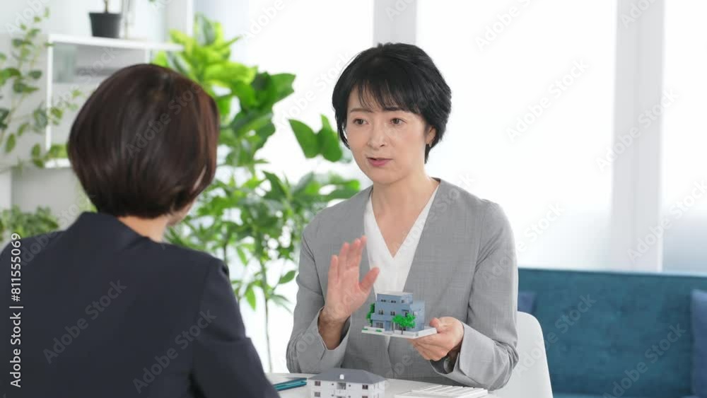 Poster オフィスで住宅模型を持って会話する二人の女性ビジネスパーソン