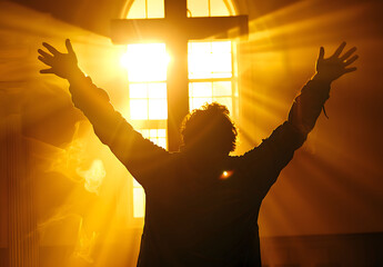 backlit image of a believer hands to heaven worshiping the cross