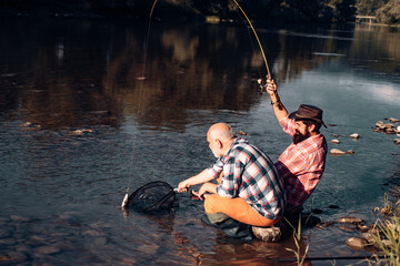 Father and mature son fisherman fishing with a fishing rod on river. Catching trout fish.