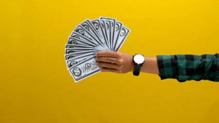 Close-up of a hand holding banknotes against a bright yellow background. Ideal for illustrating...