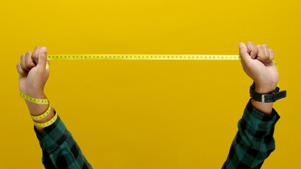 Hand holding a measuring tape against a yellow background