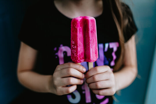 Close up of young girl holding a pink ice pop with both hands