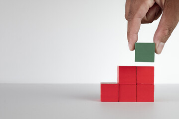 Hand choosing Green wooden cube among red wooden cubes stack as stair shape.