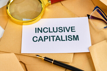 Business inclusive capitalism concept. Copy space. Words Inclusive capitalism on a blank sheet near a pen, magnifying glass and glasses