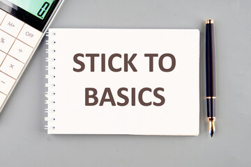 Finance and economics concept. Text STICK TO BASICS on a white notebook on a gray background