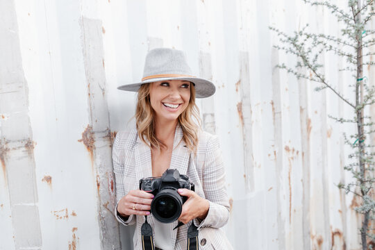 Woman with camera smiling by rustic wall
