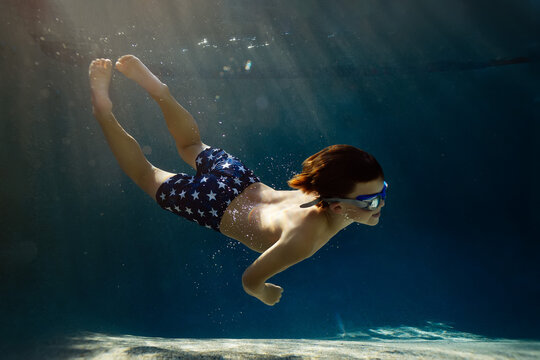Young boy swims underwater with sun dancing through the water