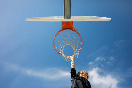 Young boy reaches for basketball hoop underneath blue sky