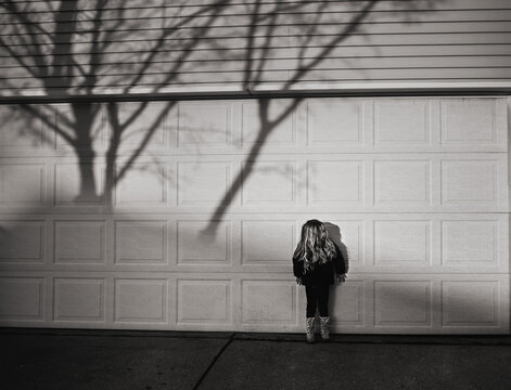 Small girl standing against garage door on sunny day