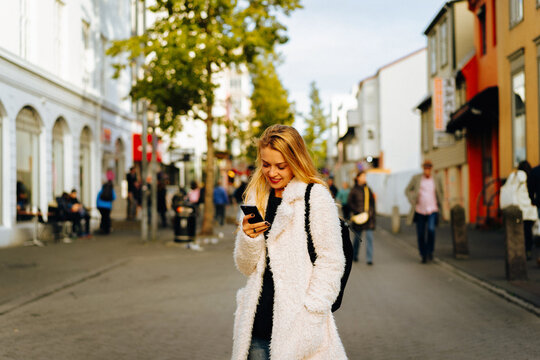 Smiling woman using mobile phone on the street.
