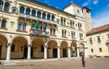 Obraz premium the woman poses in Piazza del Duomo in front of the Prefecture Palace and the clock tower in Belluno Italy