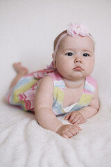 Full body figure of an infant looking at the camera while lying on his back on a white sheet bed