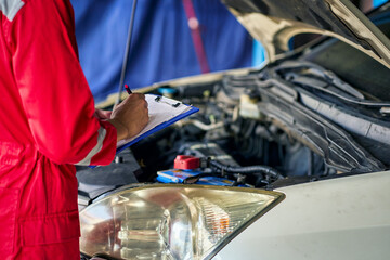 Car garage service ,  Technician in red suit checking car engine with warantee chart list.