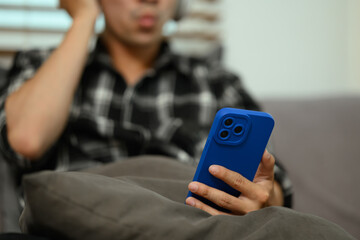 Young man listening to music with wireless headphones using mobile phone at home