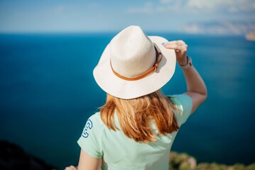 A woman wearing a straw hat is standing on a beach looking out at the ocean