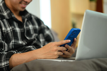 Smiling young man using smartphone, chatting to colleagues and clients over the internet