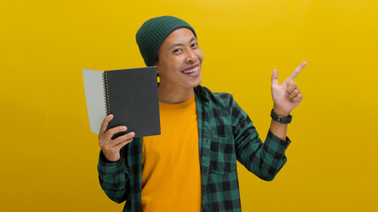 An excited young Asian student, dressed in a beanie hat and casual clothes, is smiling while...