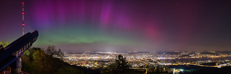 Large panorama of the city of Zurich in Switzerland from Uetliberg at night with northern lights