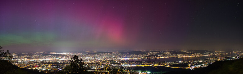 Large panorama of the city of Zurich in Switzerland from Uetliberg at night with northern lights