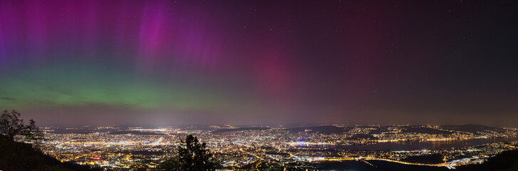 Large panorama of the city of Zurich in Switzerland from Uetliberg at night with northern lights