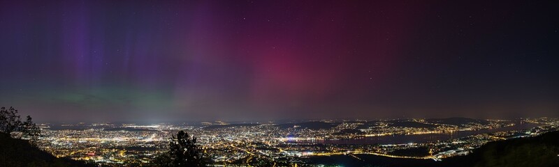 Large panorama of the city of Zurich in Switzerland from Uetliberg at night with northern lights