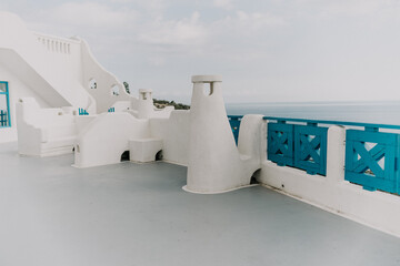 A white building with blue trim and a blue balcony. The balcony overlooks the ocean. The building...