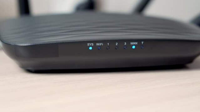 A close-up of turning on a black Wi-Fi router with antennas. The router flashes blue light.