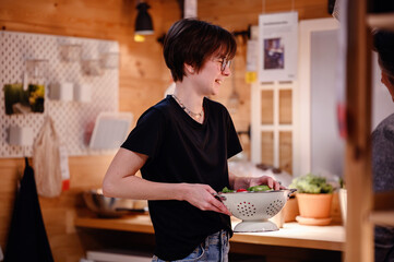 This image portrays a young adult focused on preparing fresh vegetables in a rustic kitchen. The...