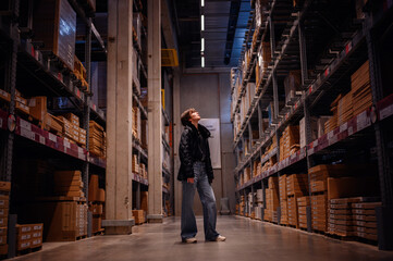 In a commanding display, a young woman stands firmly in the center of a warehouse aisle, surrounded...