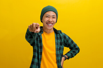 Its you. Young Asian man, dressed in a beanie hat and casual shirt, smiles while pointing his finger at the camera, choosing, inviting people, recruiting, standing over yellow background