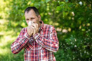 A white European man sneezes and blows his nose into a paper napkin against a green background. Spring exacerbation of allergy to poplar fluff. Allergy in adults hay fever