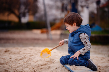 Intently focused, a young boy uses a shovel to play in the sand at a playground, illustrating a...