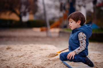 Intently focused, a young boy uses a shovel to play in the sand at a playground, illustrating a...