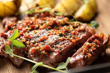 Close-up of beef steak cut into slices served with vegetable sauce and fried potatoes on a wooden...