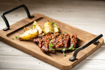 Sliced grilled meat steak Ribeye medium rare serving on wooden serving board with potatoes on table.