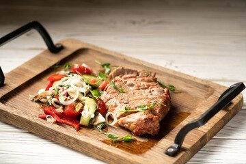 Pork steak cut into slices served with vegetables on a wooden board on a white table