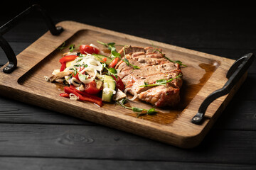 Pork steak cut into slices served with vegetables on a wooden board on a black background