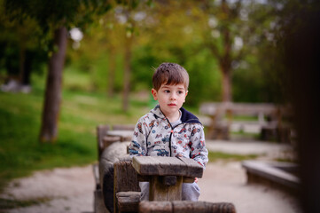 This image beautifully captures a pensive young boy sitting in a wooden structure at a park,...
